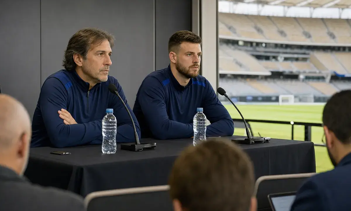 Allenatore e portiere in conferenza stampa allo stadio, seduti al tavolo con microfoni e bottiglie d’acqua