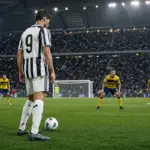 Attaccante in maglia bianconera numero 19 con il pallone, davanti a difensori gialloblù e alla porta in uno stadio pieno