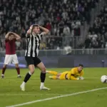 Attaccante in maglia bianconera con le mani sulla testa dopo un’occasione mancata, palla fuori di poco accanto al palo