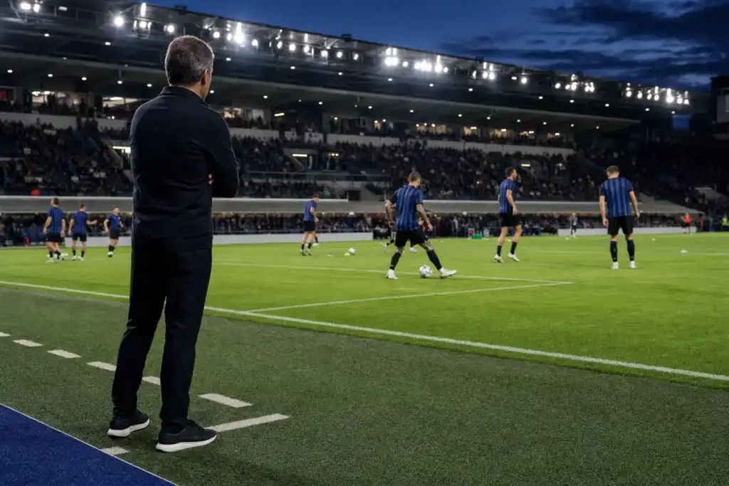 Allenatore a bordo campo osserva il riscaldamento di una squadra in maglia nerazzurra sotto i riflettori