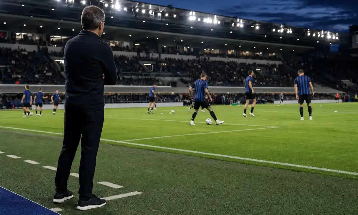 Allenatore a bordo campo osserva il riscaldamento di una squadra in maglia nerazzurra sotto i riflettori