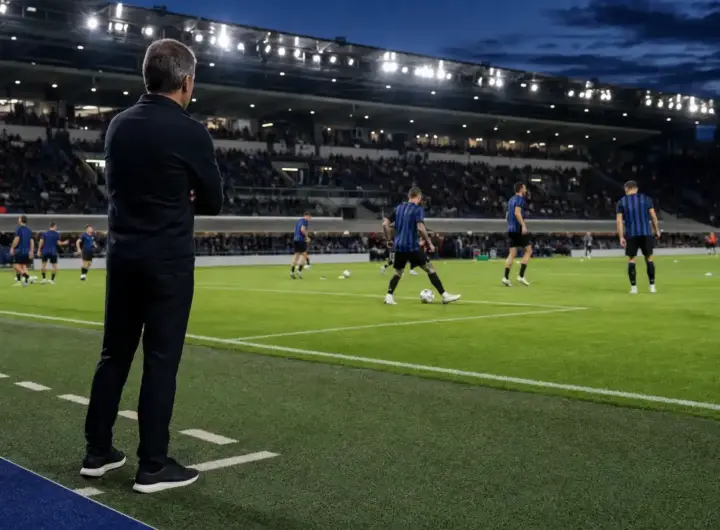 Allenatore a bordo campo osserva il riscaldamento di una squadra in maglia nerazzurra sotto i riflettori
