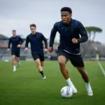 Calciatore in maglia scura a righe blu dribbla il pallone in allenamento, con compagni e allenatore sullo sfondo