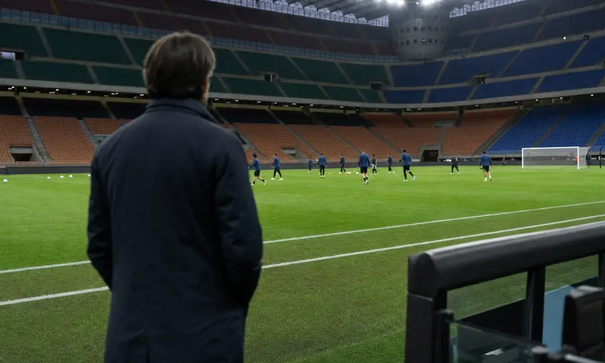 Allenatore di spalle a bordo campo mentre i giocatori si allenano in uno stadio illuminato prima della partita