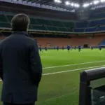 Allenatore di spalle a bordo campo mentre i giocatori si allenano in uno stadio illuminato prima della partita