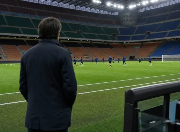 Allenatore di spalle a bordo campo mentre i giocatori si allenano in uno stadio illuminato prima della partita