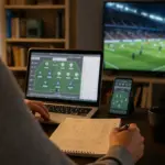 Mani che preparano la formazione al fantacalcio su laptop e smartphone, con taccuino e partita in TV sullo sfondo