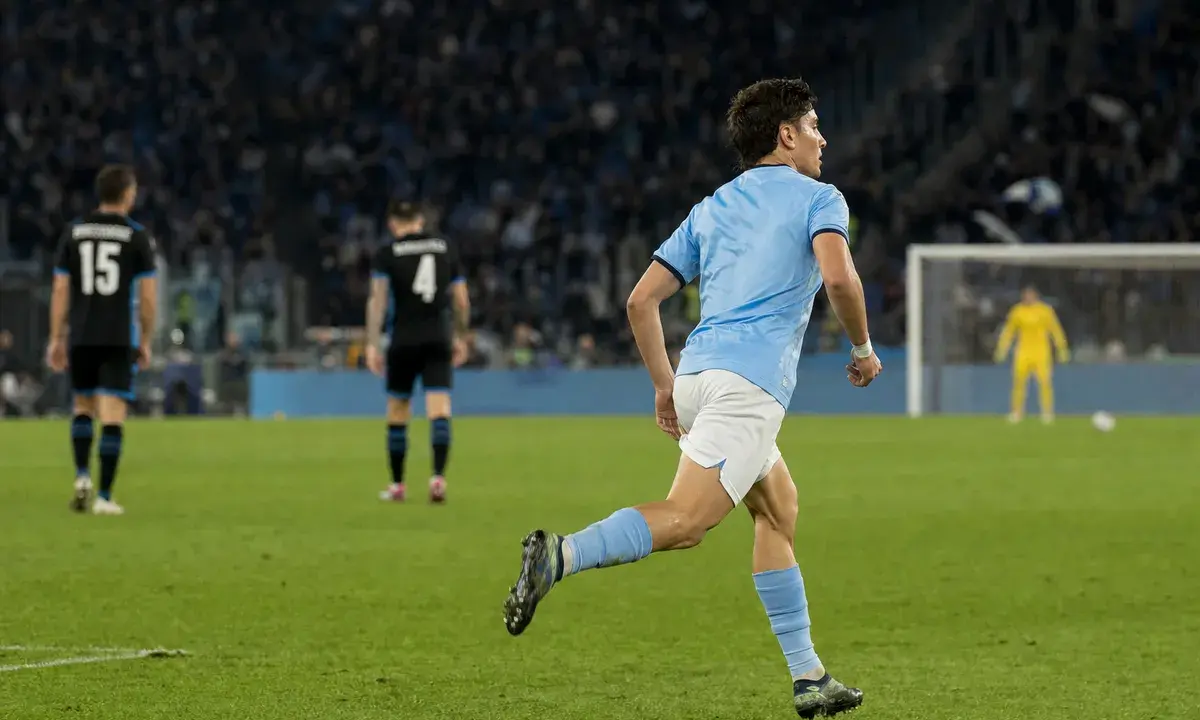 Centrocampista in maglia azzurro chiaro corre verso l’area di rigore in uno stadio illuminato di sera