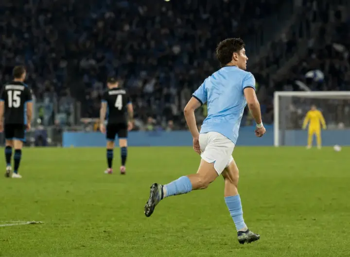 Centrocampista in maglia azzurro chiaro corre verso l’area di rigore in uno stadio illuminato di sera