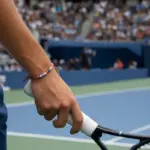 Polso di un tennista con braccialetto di perline colorate mentre impugna la racchetta su un campo in cemento