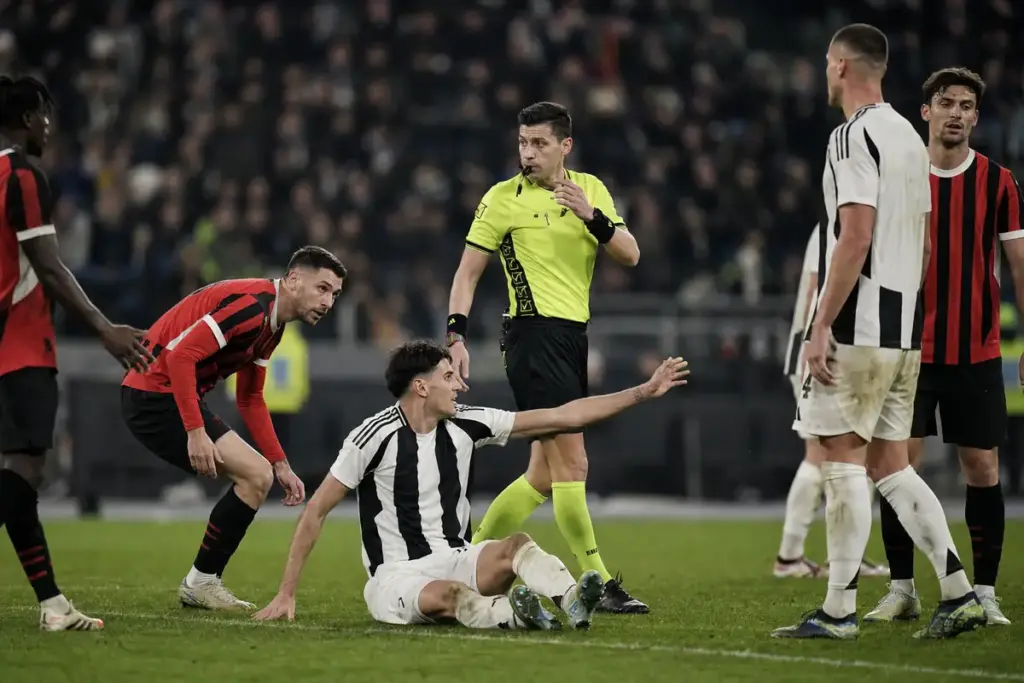 Arbitro in maglia gialla valuta un contatto in area mentre un giocatore bianconero è a terra e protesta