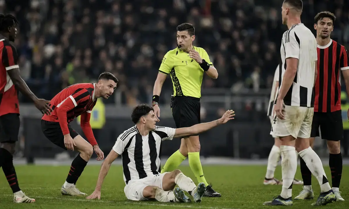 Arbitro in maglia gialla valuta un contatto in area mentre un giocatore bianconero è a terra e protesta