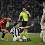 Arbitro in maglia gialla valuta un contatto in area mentre un giocatore bianconero è a terra e protesta