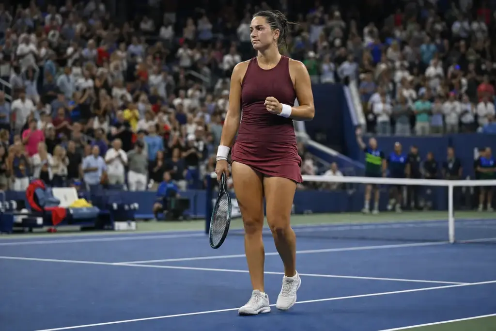 Tennista su campo in cemento blu, racchetta in mano e pugno chiuso, con il pubblico in piedi sugli spalti