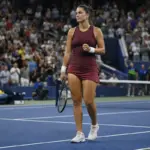 Tennista su campo in cemento blu, racchetta in mano e pugno chiuso, con il pubblico in piedi sugli spalti