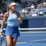 Tennista in campo su cemento blu durante un match, con rete in primo piano e pubblico sfocato sugli spalti